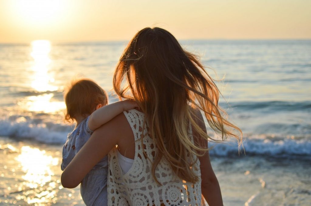 mother on beach holding child looking to horizon