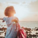 woman arms outstretched on beach, sun ahead
